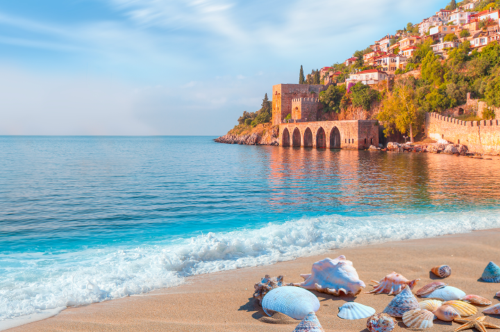 Sandstrand mit Muscheln und einer beeindruckenden Burg im Hintergrund, gelegen in Antayla.
