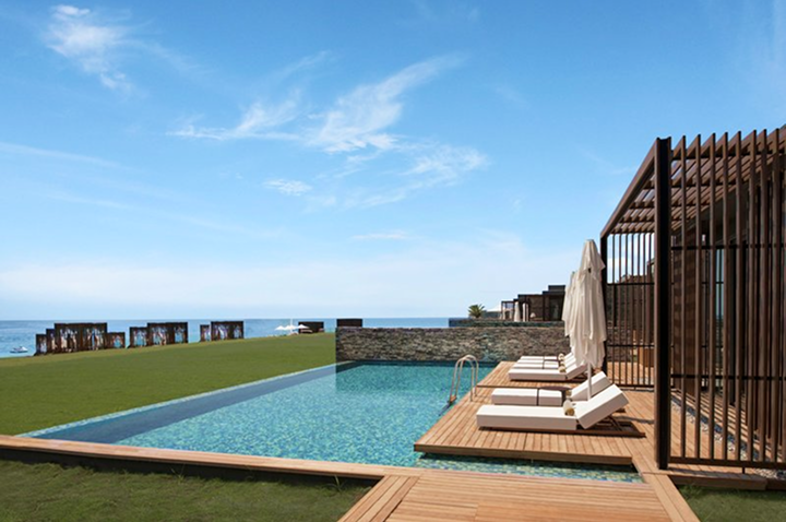 Infinity-Pool mit Liegestühlen und Sonnenschirmen auf Holzdeck neben Meerblick.