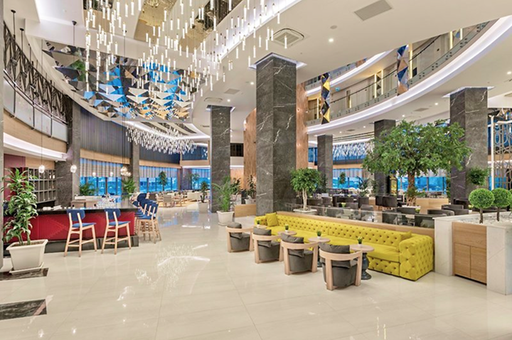 Großer Außenpool vor einem mehrstöckigen Hotelgebäude mit Balkonen und Palmen am Rand.