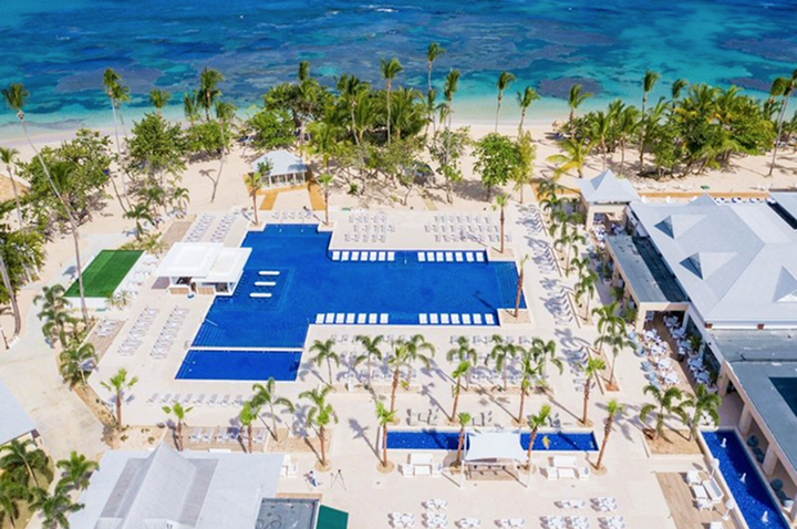 Luftaufnahme eines großen rechteckigen Pools mit Liegestühlen und Palmen, dahinter türkisfarbenes Meer und Strand. Luftaufnahme eines großen rechteckigen Pools mit Liegestühlen und Palmen, dahinter türkisfarbenes Meer und Strand.