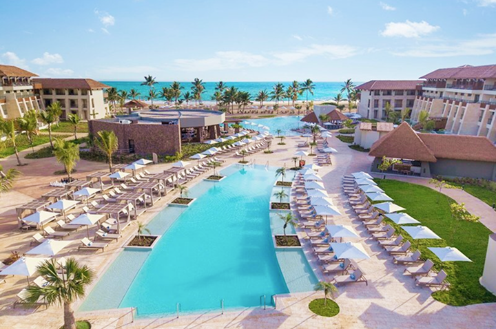 Großer Hotelpool mit Liegen und Sonnenschirmen, umgeben von mehrstöckigen Hotelgebäuden und Palmen, im Hintergrund das Meer. Großer Hotelpool mit Liegen und Sonnenschirmen, umgeben von mehrstöckigen Hotelgebäuden und Palmen, im Hintergrund das Meer.