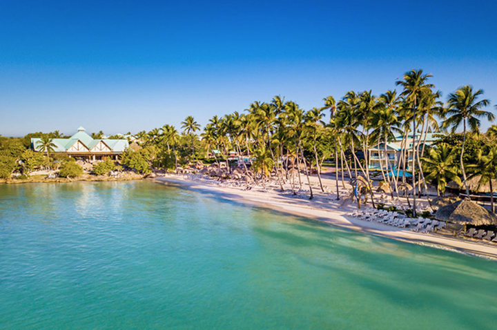 Strand mit Palmen und mehreren Gebäuden am Ufer eines ruhigen, türkisfarbenen Meeres unter klarem Himmel. Strand mit Palmen und mehreren Gebäuden am Ufer eines ruhigen, türkisfarbenen Meeres unter klarem Himmel.