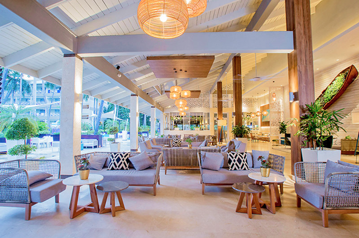 Offener, heller Lounge-Bereich mit modernen Sitzmöbeln, Holztischen, Pflanzen und hängenden Lampen unter einem weißen Satteldach. Offener, heller Lounge-Bereich mit modernen Sitzmöbeln, Holztischen, Pflanzen und hängenden Lampen unter einem weißen Satteldach.