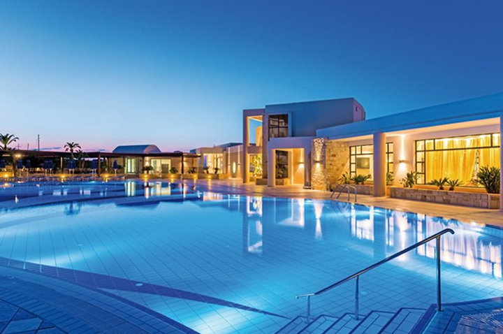 Großer beleuchteter Hotelpool mit moderner Architektur im Hintergrund bei Dämmerung.