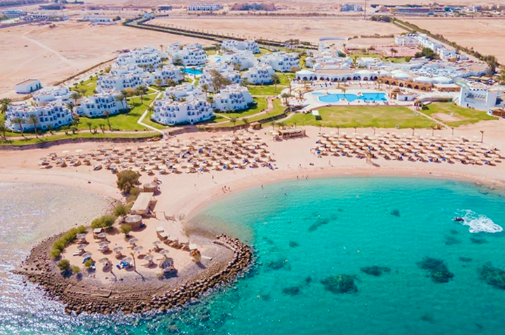 Luftaufnahme eines Strandes mit einem luxuriösen Resort, umgeben von klarem Wasser und üppigem Grün.