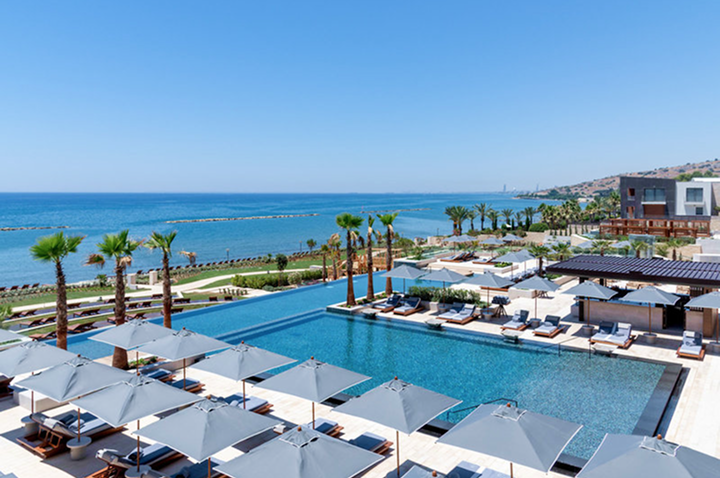 Hotelpool mit Liegen und Sonnenschirmen vor Meer und Küstenlandschaft.