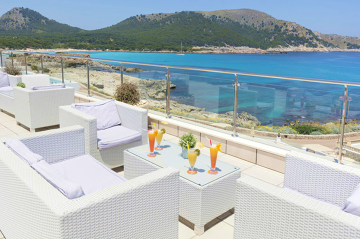 Stilvolle weiße Terrasse mit Wicker-Möbeln, die den Blick auf den weiten Ozean freigibt.