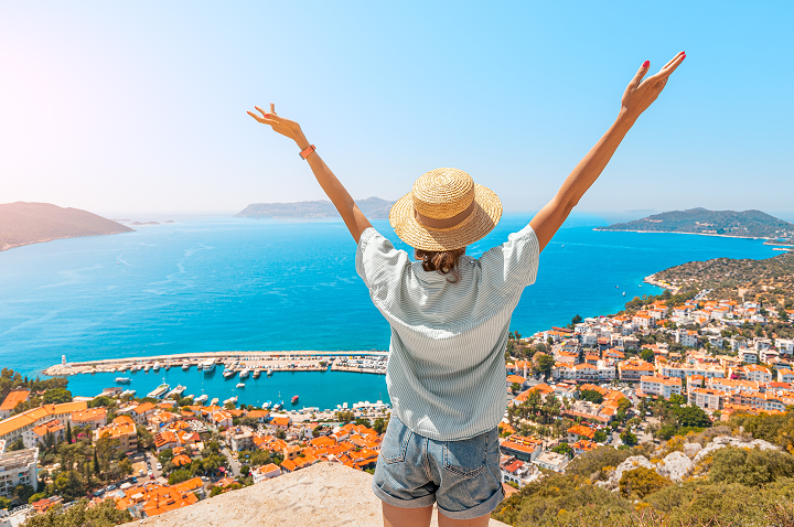 Eine Frau mit erhobenen Armen blickt auf das Meer und die Stadt im Hintergrund.